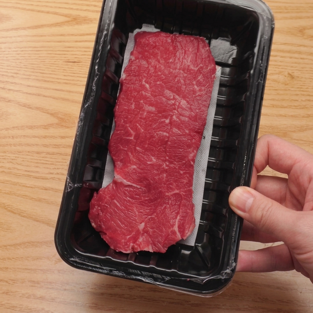 Filet de bœuf cru coupé en cubes uniformes sur une planche à découper en bois.