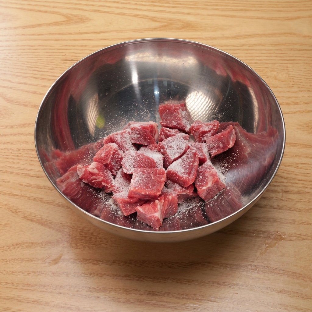 Cubes de bœuf dans un bol mélangeur en métal, enrobés de sel, sucre, sauce soja et fécule.