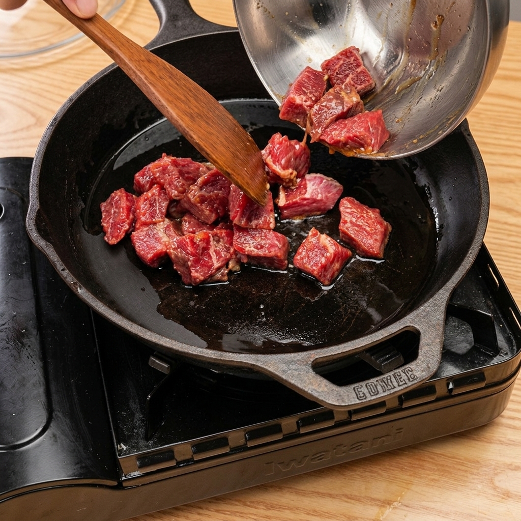 Cubes de bœuf dorant dans une poêle en fonte, avec de la vapeur séchappant après lajout de vin de cuisine et le couvert.
