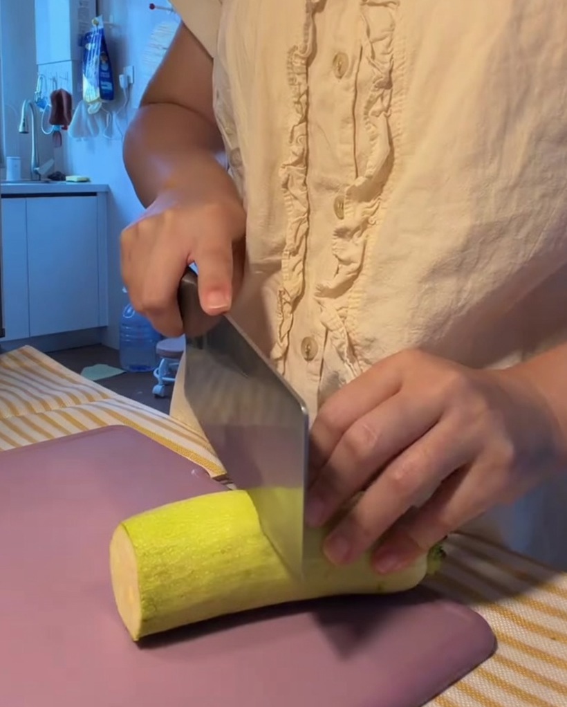 Courgette fraîche coupée en demi-lunes régulières sur une planche à découper violette.
