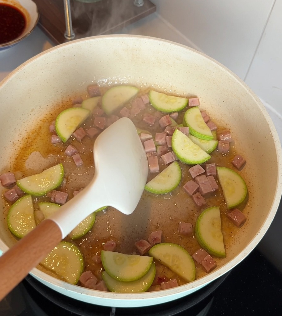 Tranches de courgettes et cubes de viande sautant ensemble dans une poêle antiadhésive.