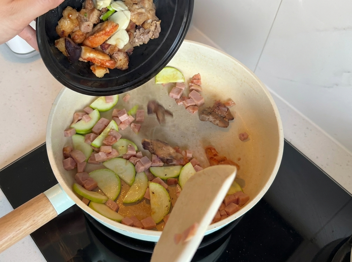 Une poêle contenant des courgettes et de la viande sautées avec des oignons verts, de lail et des morceaux de viande cuite.