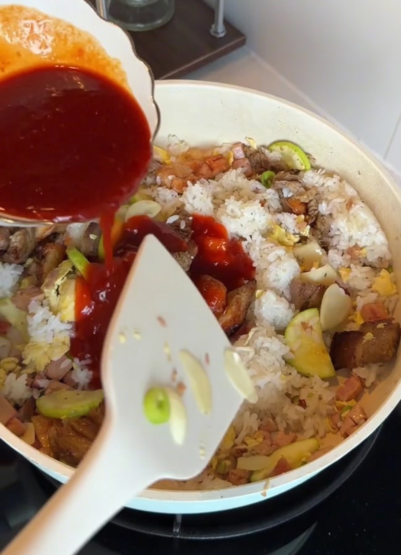 Sauce bibimbap coréenne versée sur le riz et les ingrédients dans une poêle.