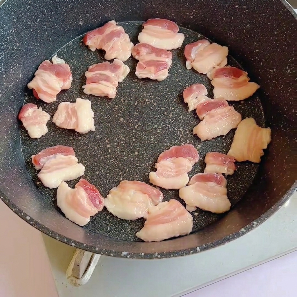 Tranches de poitrine de porc crue disposées dans une poêle chaude, commençant à dorer.