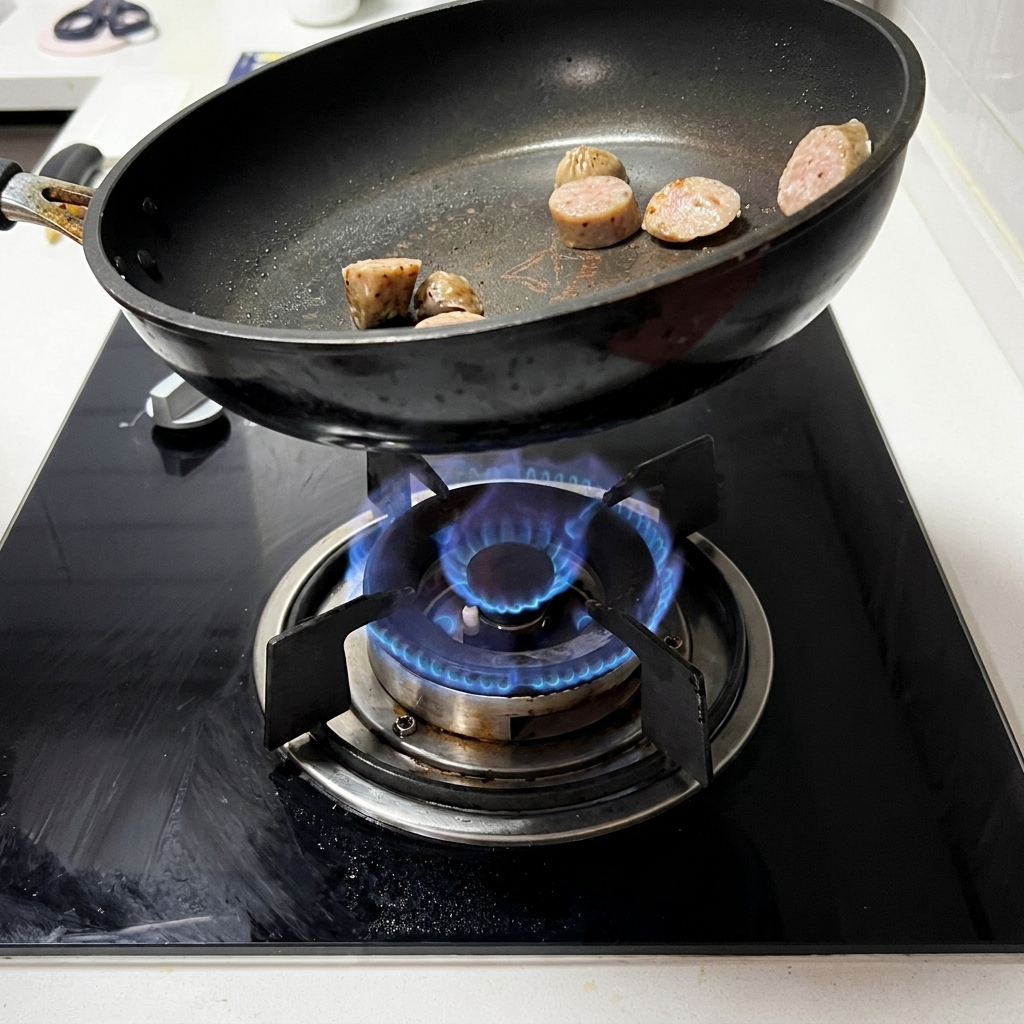 Tranches de saucisse saisies et dorées dans une poêle noire sur une cuisinière à gaz.