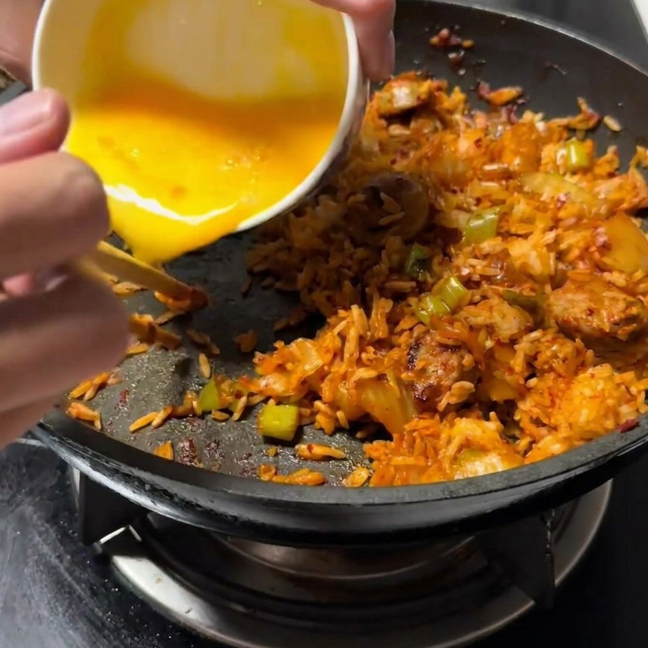 Lœuf battu versé sur un côté de la poêle, à côté du mélange de riz sauté.