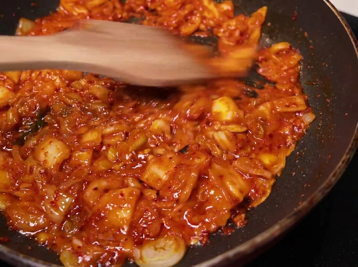 Le mélange de kimchi sauté dans une poêle avec une spatule en bois.