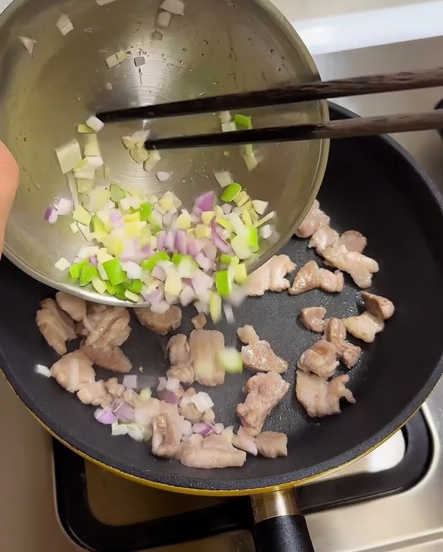 Oignons verts, ail et oignons hachés versés dans une poêle avec le porc cuit.