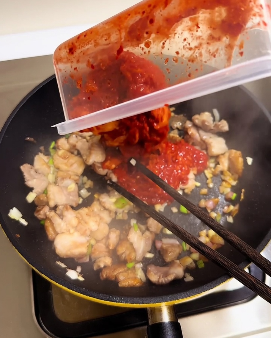 Kimchi rouge haché versé dans une poêle avec le porc et les aromates.