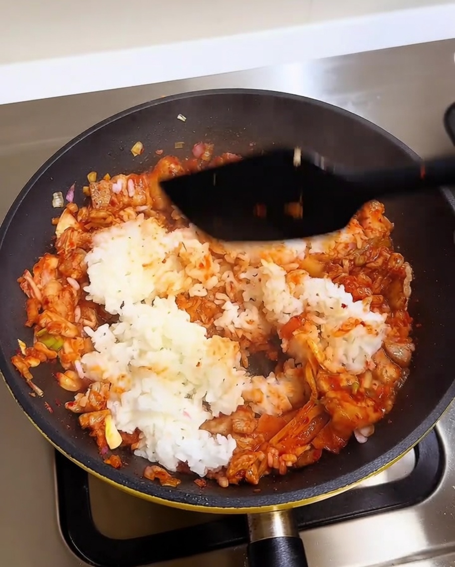 Une spatule mélangeant le riz blanc dans une base de porc et kimchi vibrante.