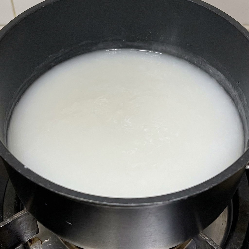 Une pâte de farine de riz gluant épaisse et blanche cuisant dans une casserole noire.