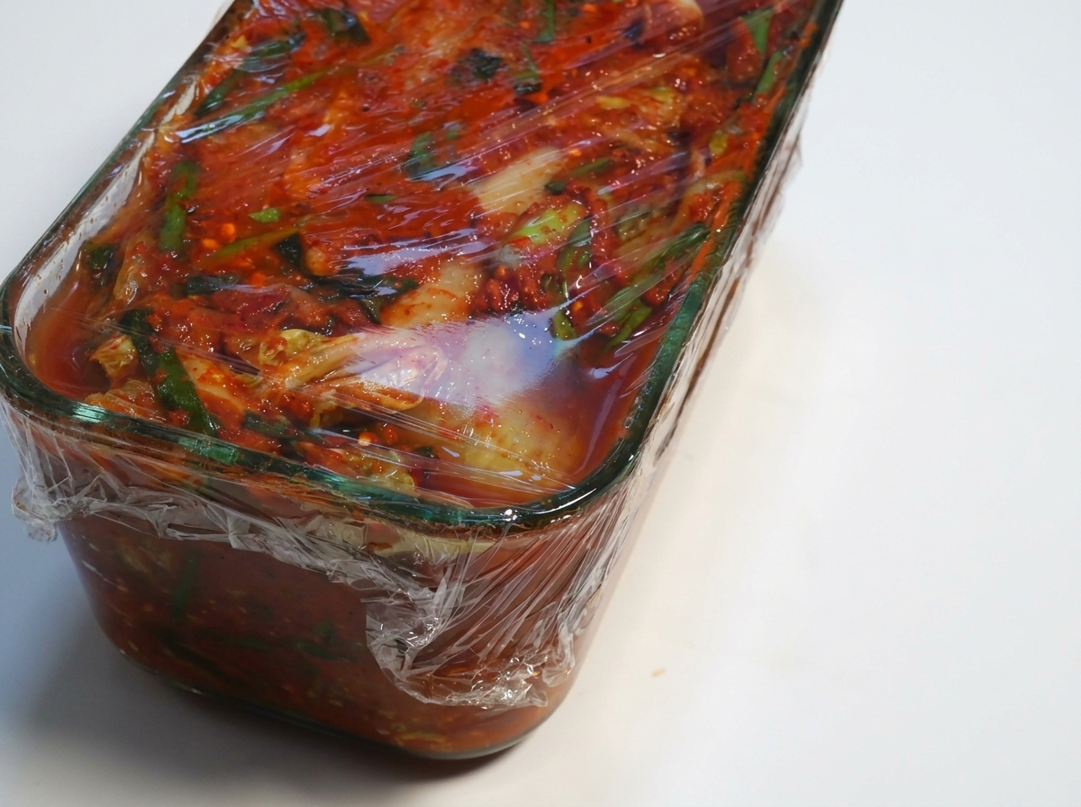 Récipient de kimchi fermenté avec le film plastique en cours de retrait.
