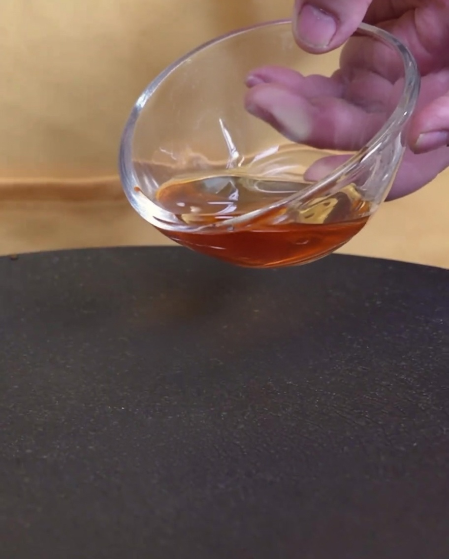 Un gros plan dhuile de sésame versée depuis un bol en verre dans une poêle chaude vide.