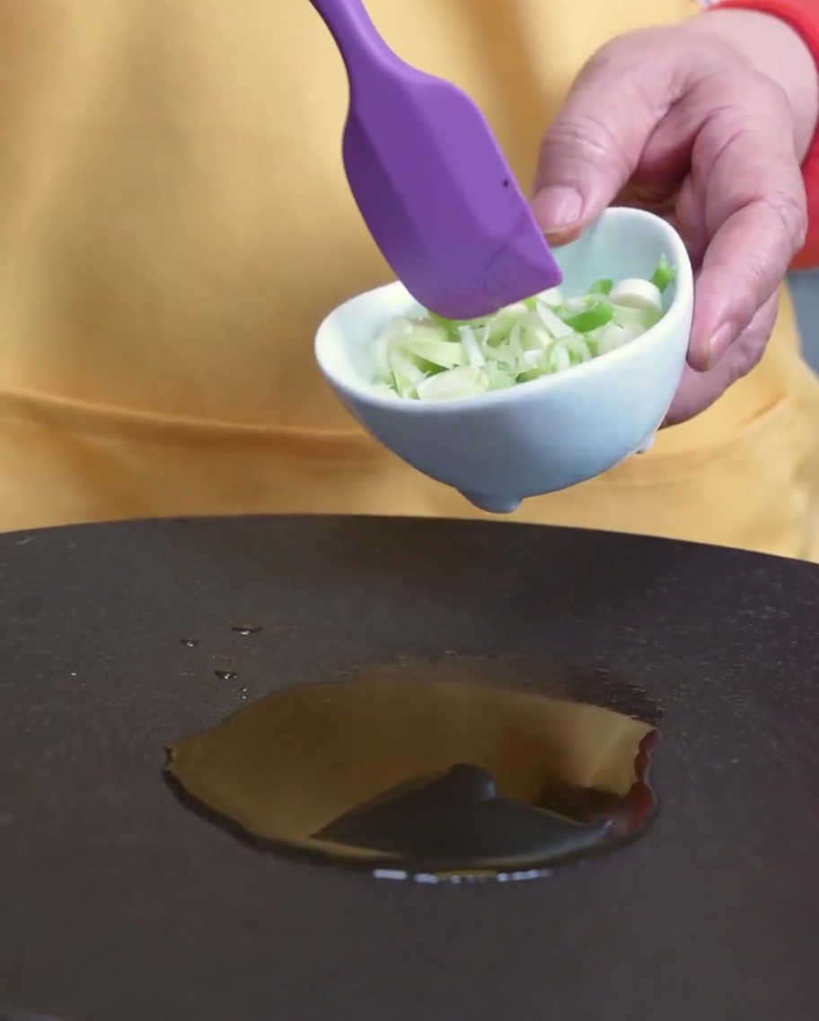 Oignons verts en train dêtre sautés dans une poêle avec de lhuile de sésame.