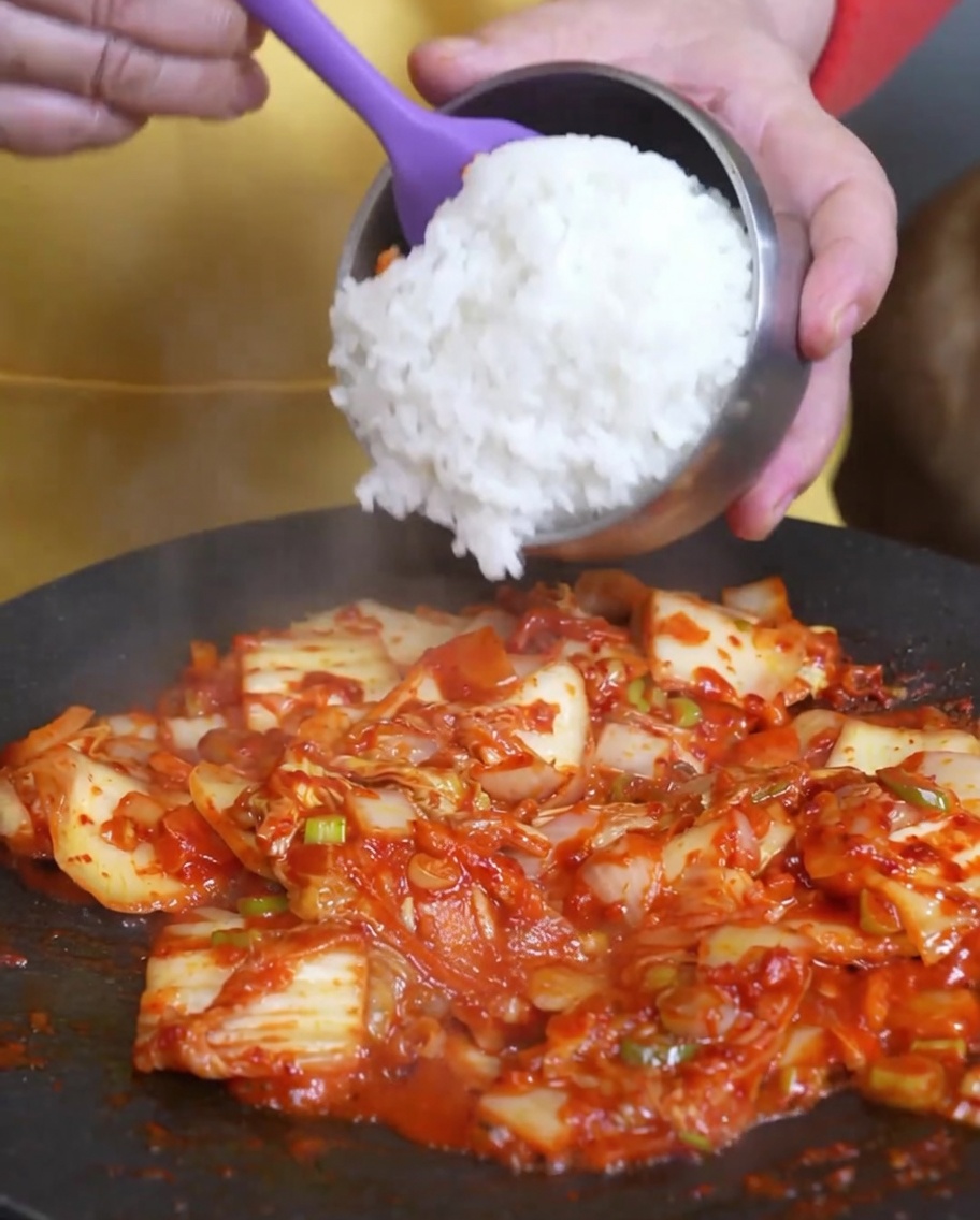 Riz blanc cuit ajouté dans la poêle contenant le kimchi sauté.