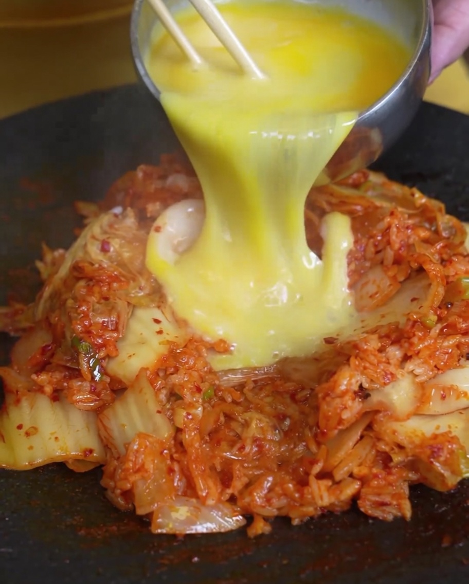 Œufs battus versés sur une portion de riz sauté au kimchi dans une poêle chaude.