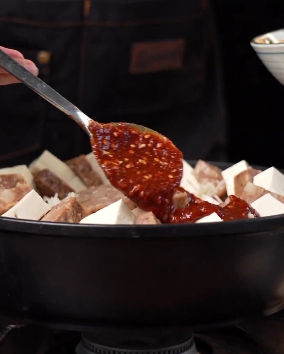 Une sauce épaisse rouge épicée versée et étalée sur les ingrédients dans une marmite en métal.