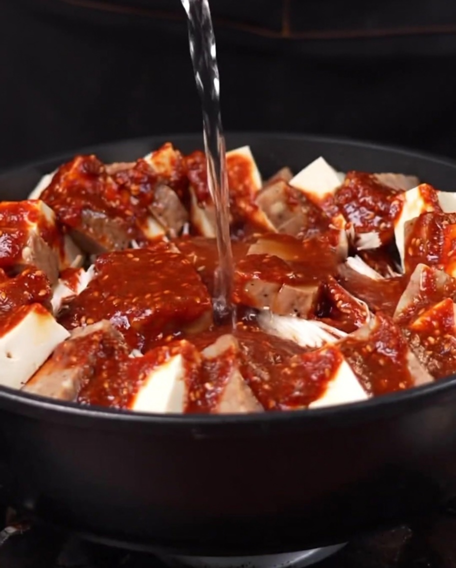 De leau bouillante versée dans la marmite, commençant à se mélanger avec la sauce et les ingrédients.