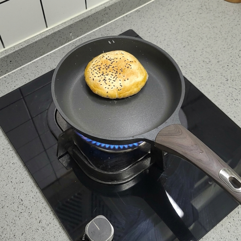 Un pain à burger surgelé aux graines de sésame cuisant à sec dans une poêle antiadhésive sur le feu.