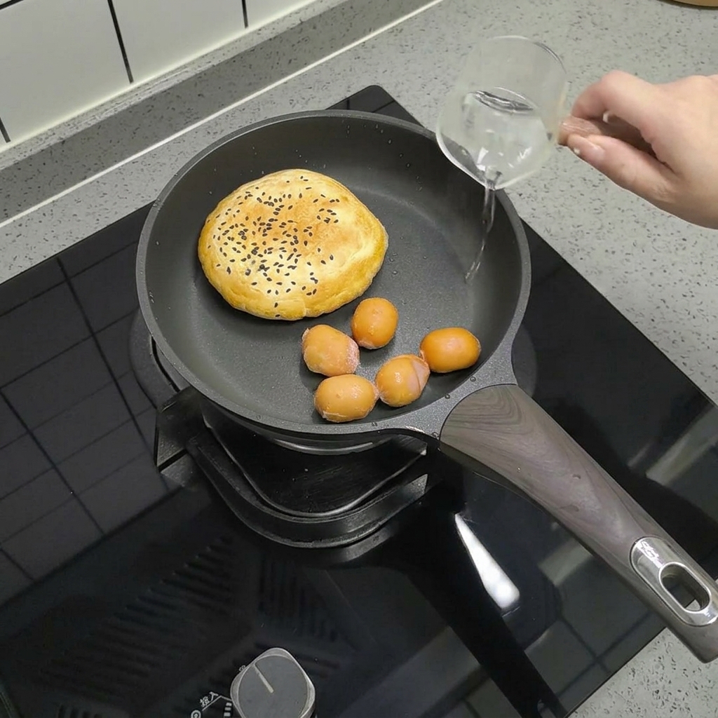 De petites saucisses disposées dans la poêle avec le pain, tandis quon y verse un fond deau avec un verre doseur.