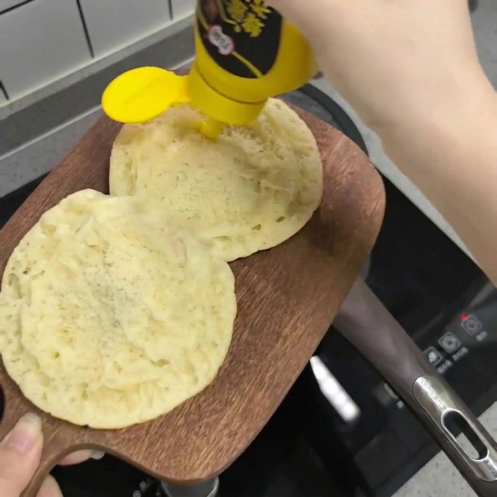 De la sauce moutarde et miel versée en filet sur les moitiés de pain à burger posées sur une planche en bois.