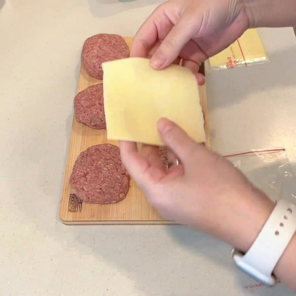 Une tranche de fromage pliée placée au centre dun steak de viande hachée aplati.