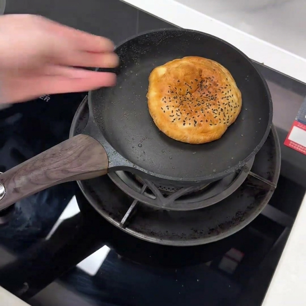 Une main place un bun au sésame noir dans une poêle antiadhésive.