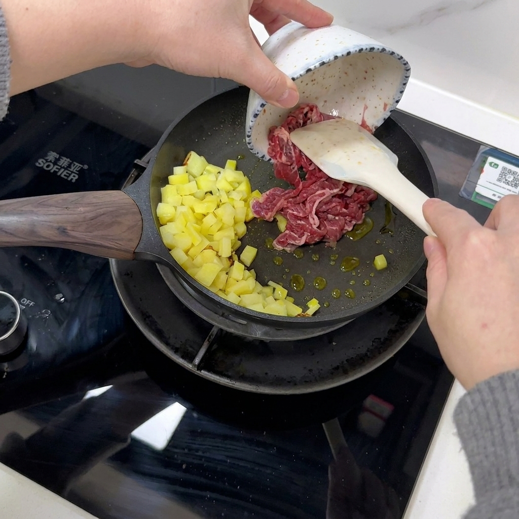 Des tranches de bœuf sont ajoutées à la poêle avec les pommes de terre cuites.