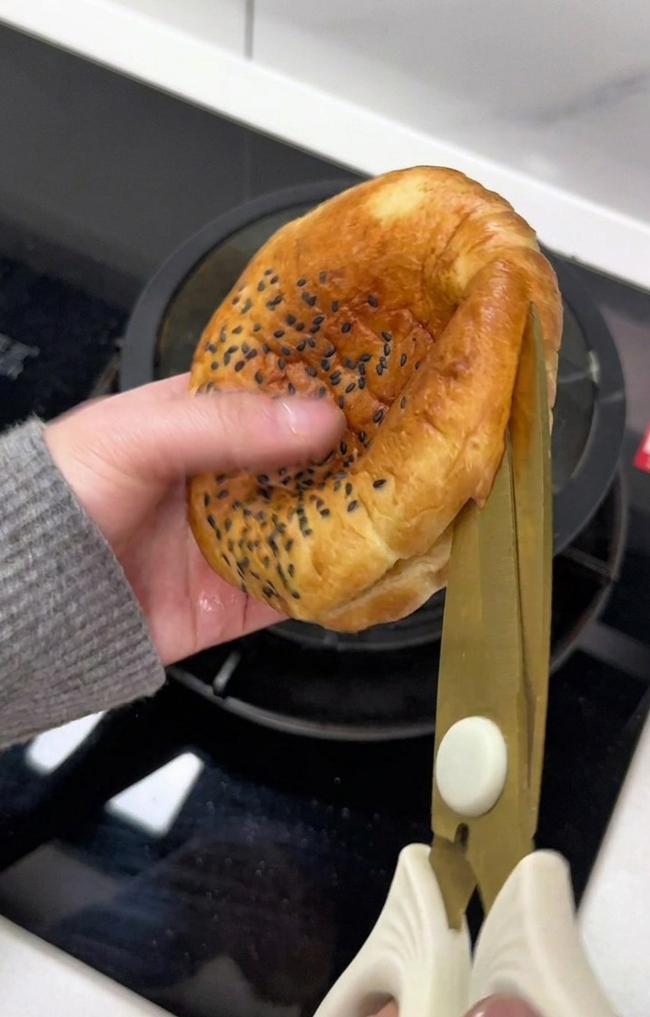 Une main utilise des ciseaux pour ouvrir un bun au sésame.