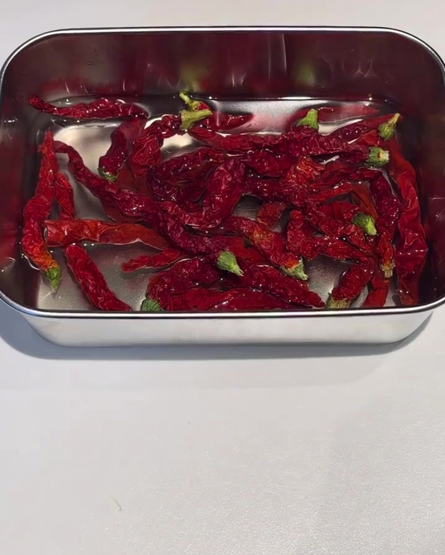 Écorces de piment rouge séché trempant dans un récipient en inox rempli deau chaude.