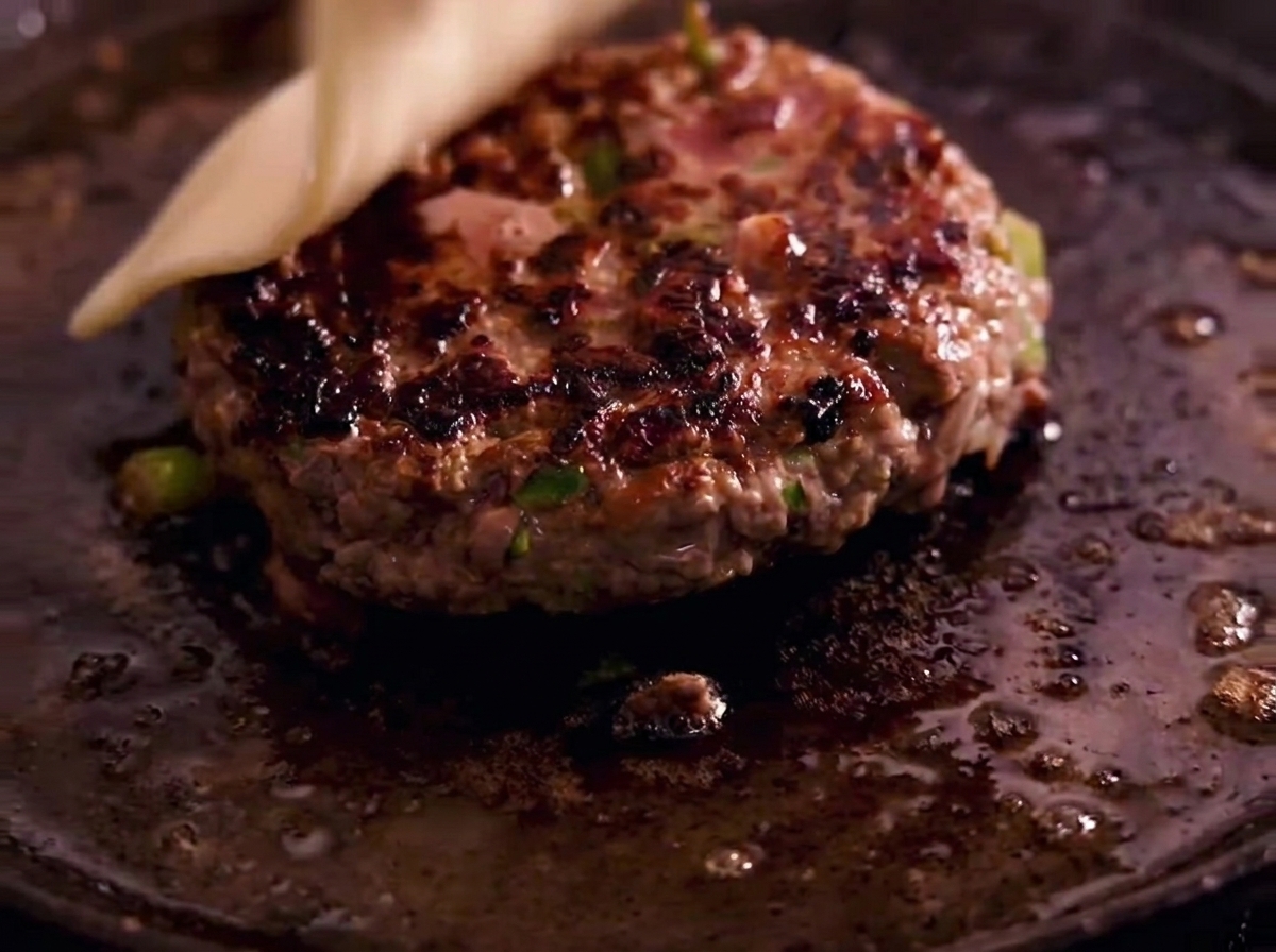Une tranche de fromage blanc fondant sur un steak juteux dans une poêle en fonte.