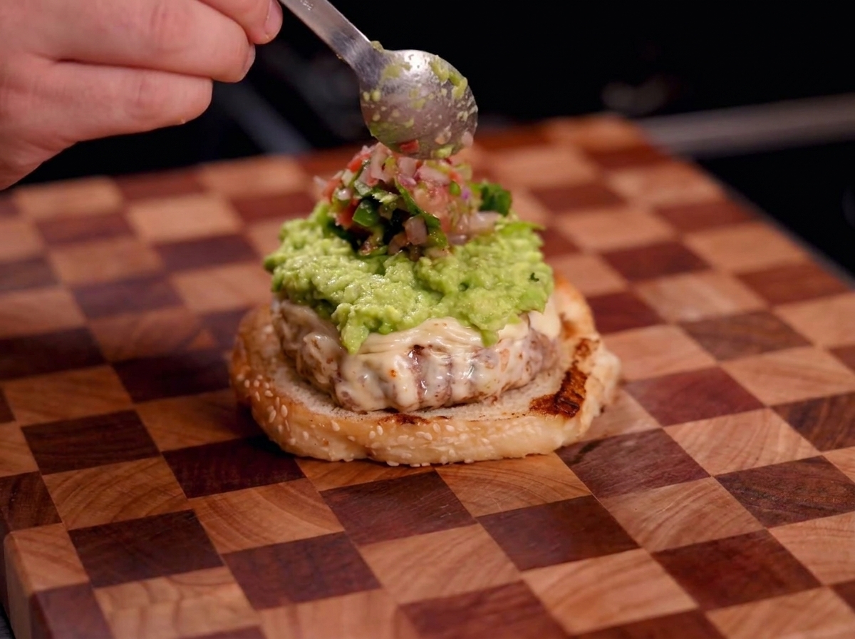Main utilisant une cuillère pour ajouter de la salsa rouge sur le guacamole.
