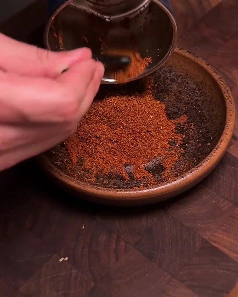 Un moulin à épices versant de la poudre de piment et dépices rouge vif fraîchement moulue dans un bol en céramique.