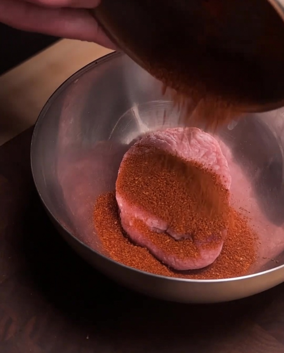 Porc haché frais dans un bol en acier inoxydable avec une couche de poudre dépices rouge versée par-dessus.