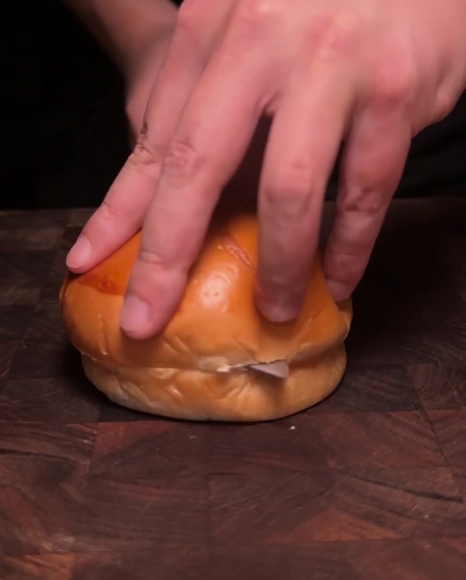 Deux moitiés de pain à burger face vers le bas dans une poêle, en train de griller dans du beurre fondu jusquà ce quelles soient dorées.
