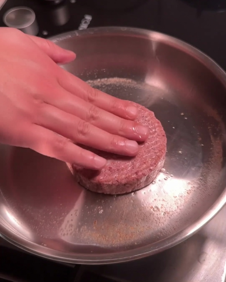 Un steak de bœuf cru étant pressé dans une poêle chaude en acier inoxydable pour la saisie.