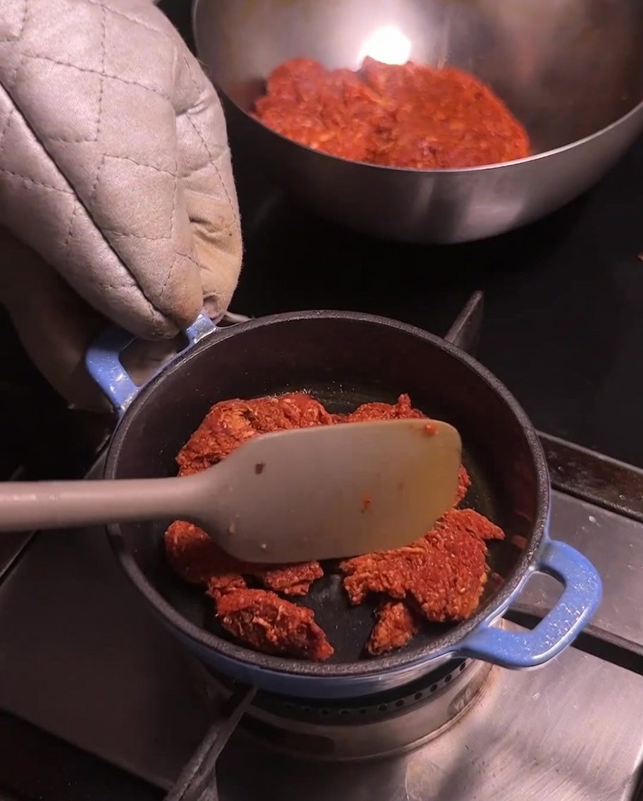 Une petite casserole bleue sur une plaque de cuisson avec du porc chorizo émietté remué avec une spatule de couleur claire.