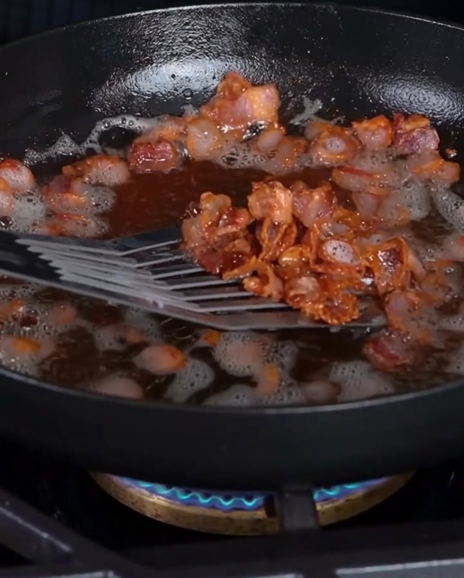 Des morceaux de bacon croustillants retirés dune poêle avec une spatule ajourée.