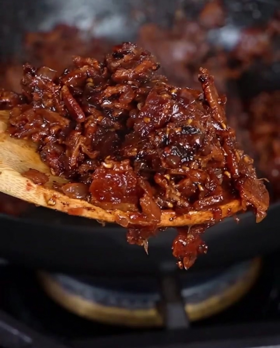 Une cuillère en bois soulevant une portion de confiture de bacon maison épaisse et dun brun rougeâtre foncé.