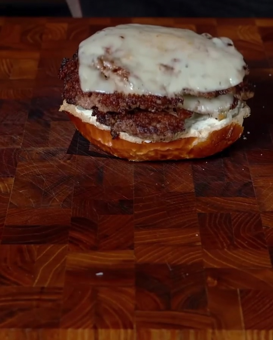 Superposition délicate de deux steaks de smashburger avec jalapeños et fromage fondu sur un pain du bas enduit de fromage à la crème.