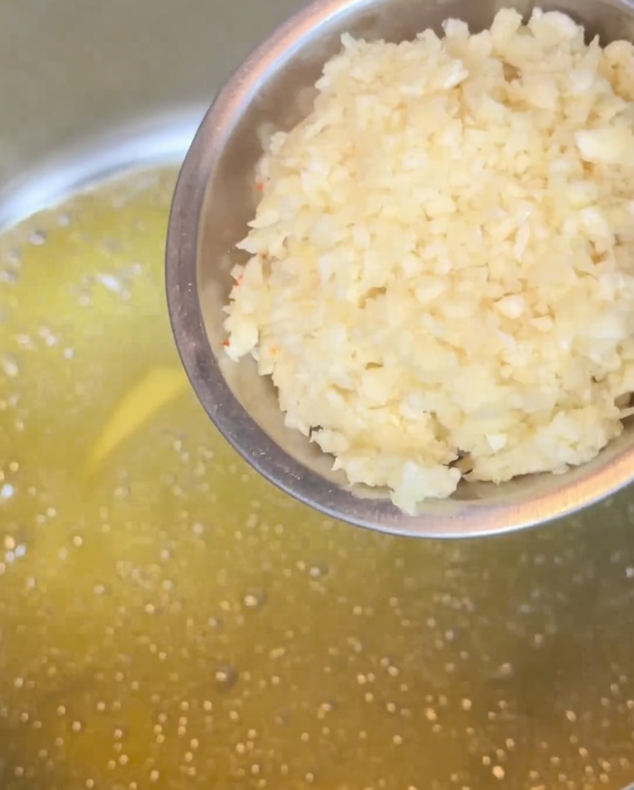 Ail émincé cuisant dans du beurre fondu dans une casserole, prenant une couleur dorée.