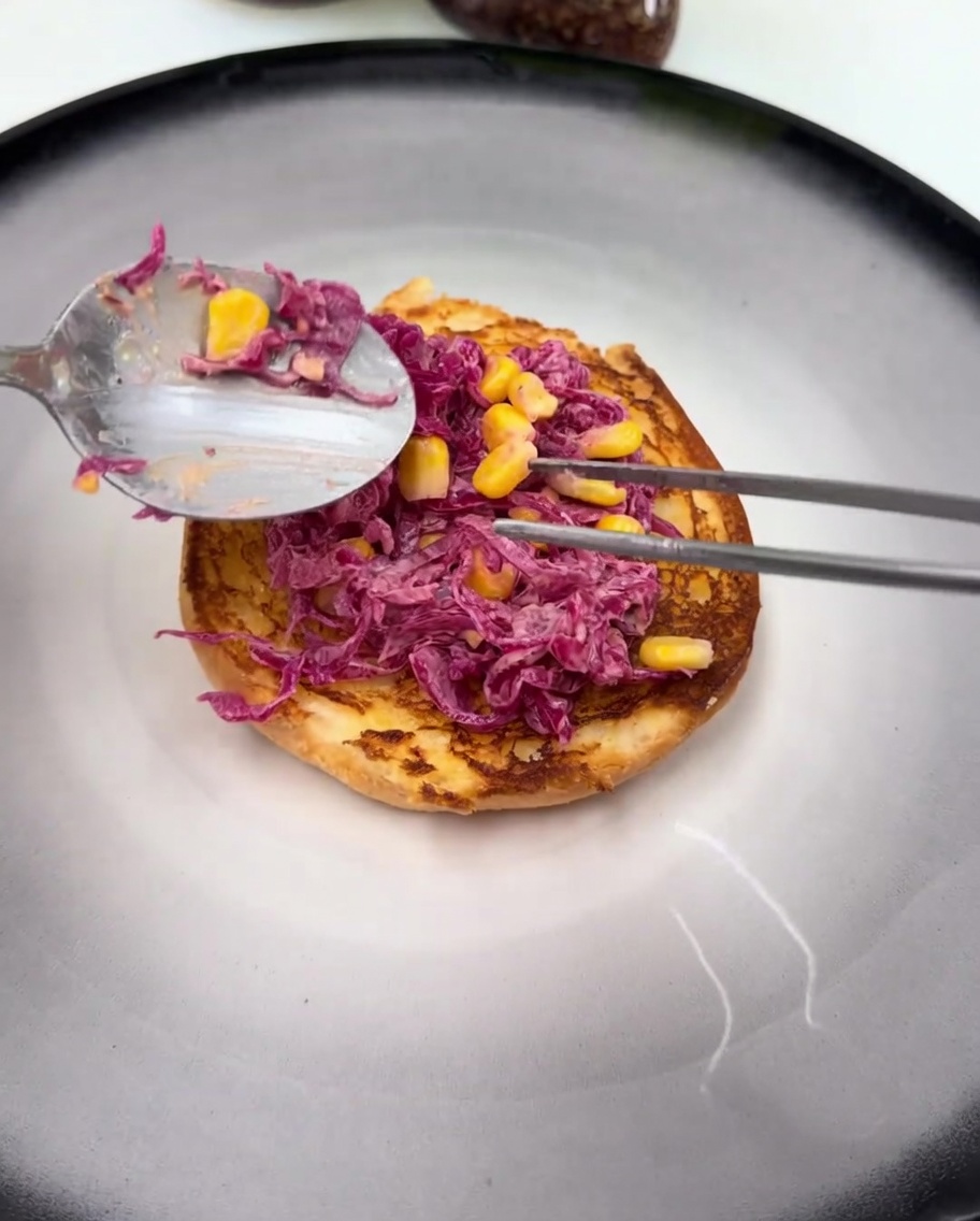 Un haut de cuisse de poulet frit glacé reposant sur la salade de chou rouge sur le pain inférieur.