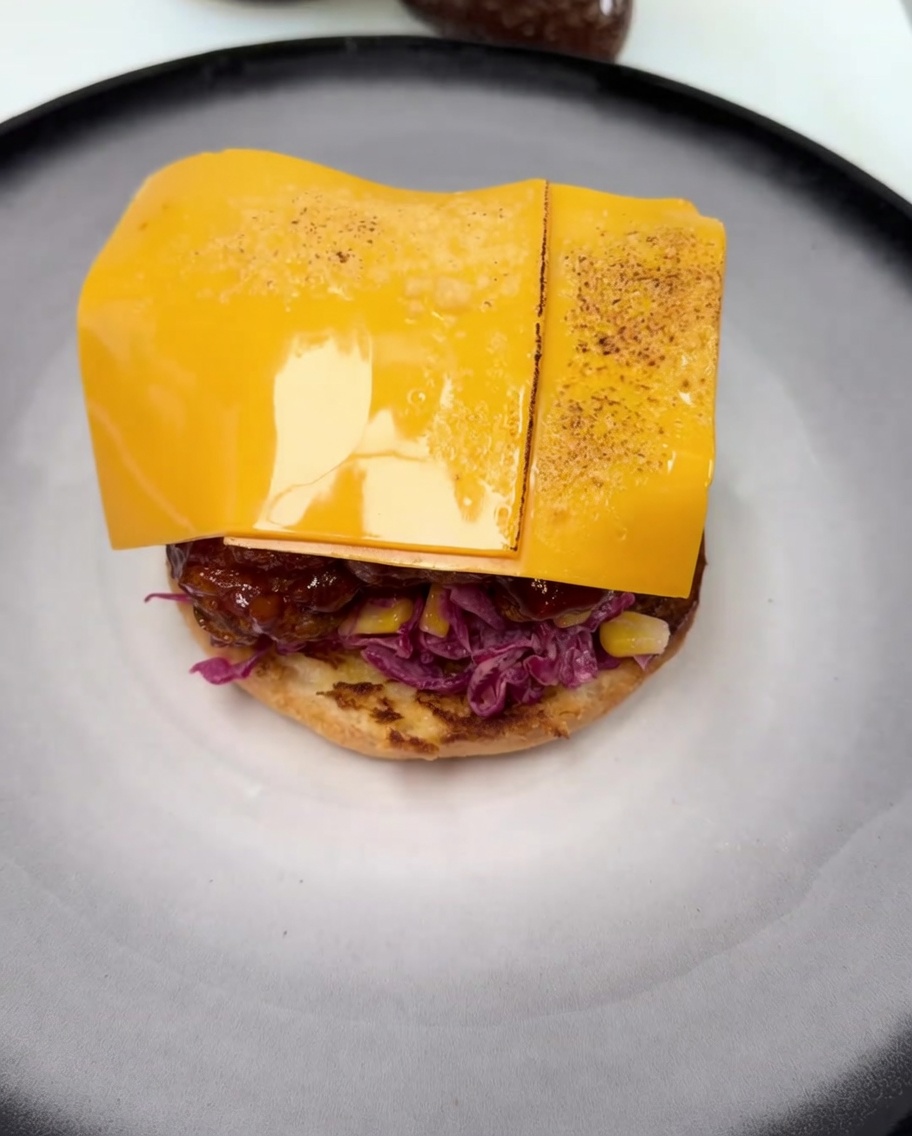 Une tranche de cheddar fondant sur le poulet frit glacé, avec des marques de brunissement dues au chalumeau.