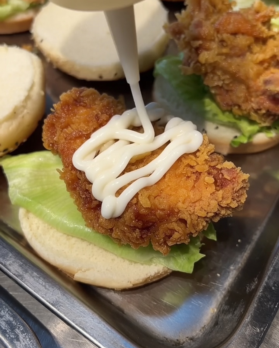 Mayonnaise blanche pressée dun flacon sur un morceau de poulet frit reposant sur un pain burger.