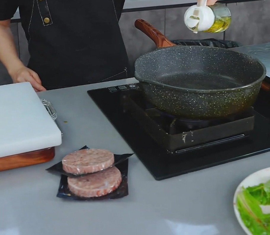 Une personne versant un filet dhuile de cuisson dans une poêle antiadhésive sombre sur la cuisinière.
