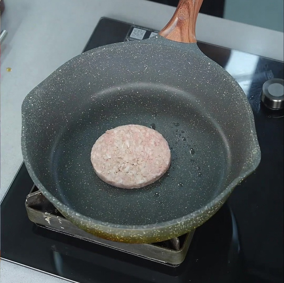 Un steak de bœuf cru commençant à grésiller dans une poêle légèrement huilée sur un brûleur.