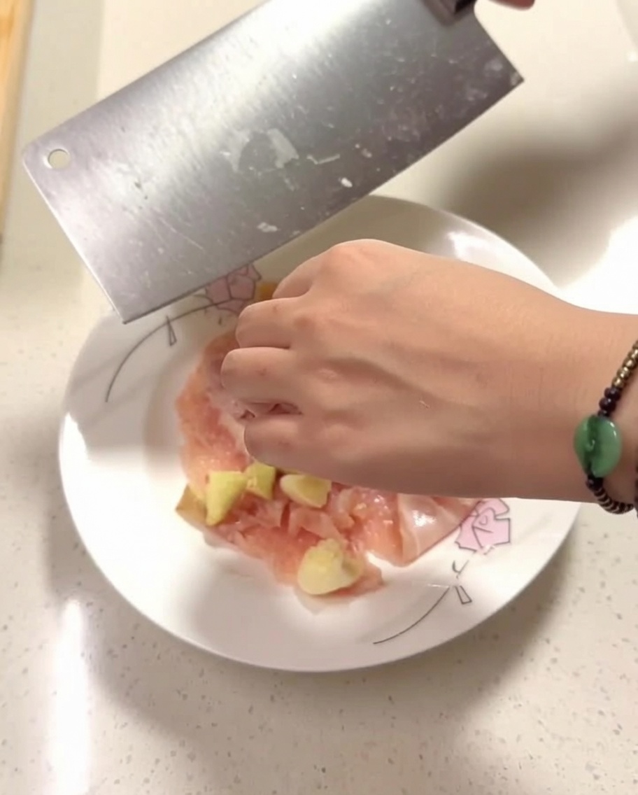 Morceaux de poulet cru sur une assiette assaisonnés de gingembre, dail et dépices.