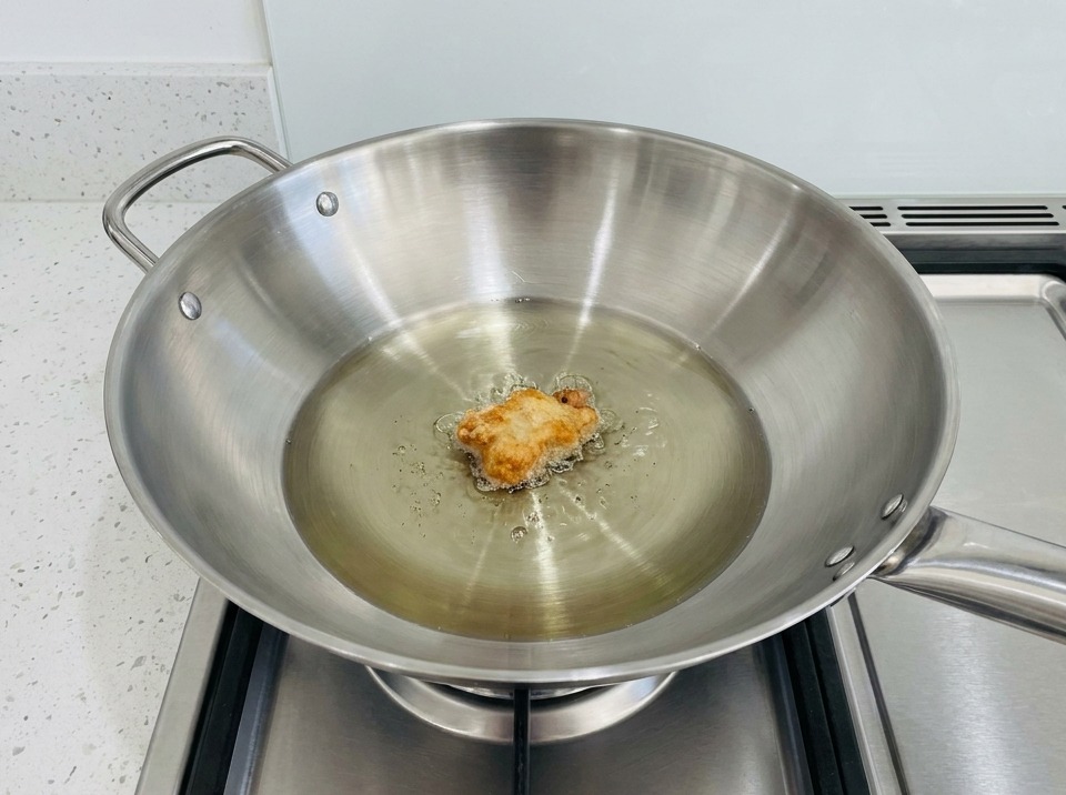 Un morceau de poulet pané en train de frire dans un wok rempli dhuile chaude.