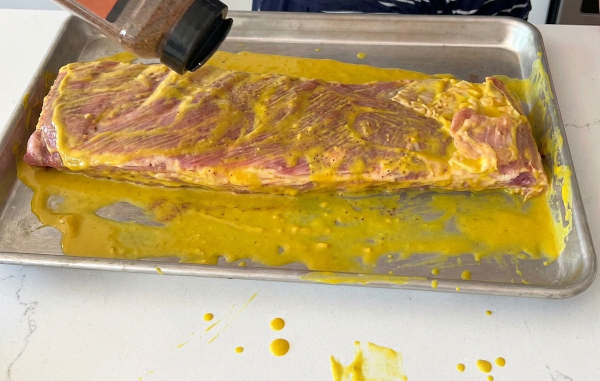 Saupoudrage dun mélange dépices sèches pour BBQ sur des travers de porc badigeonnés de moutarde.