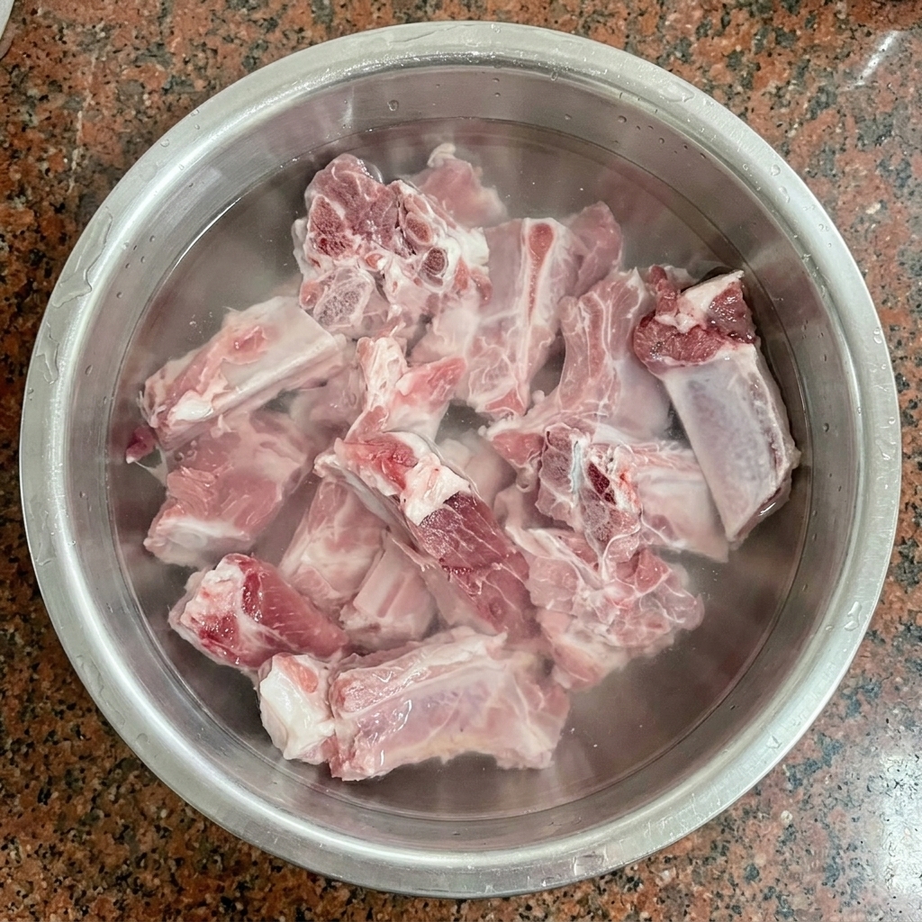 Travers de porc crus trempant dans de leau froide à lintérieur dun bol en inox.